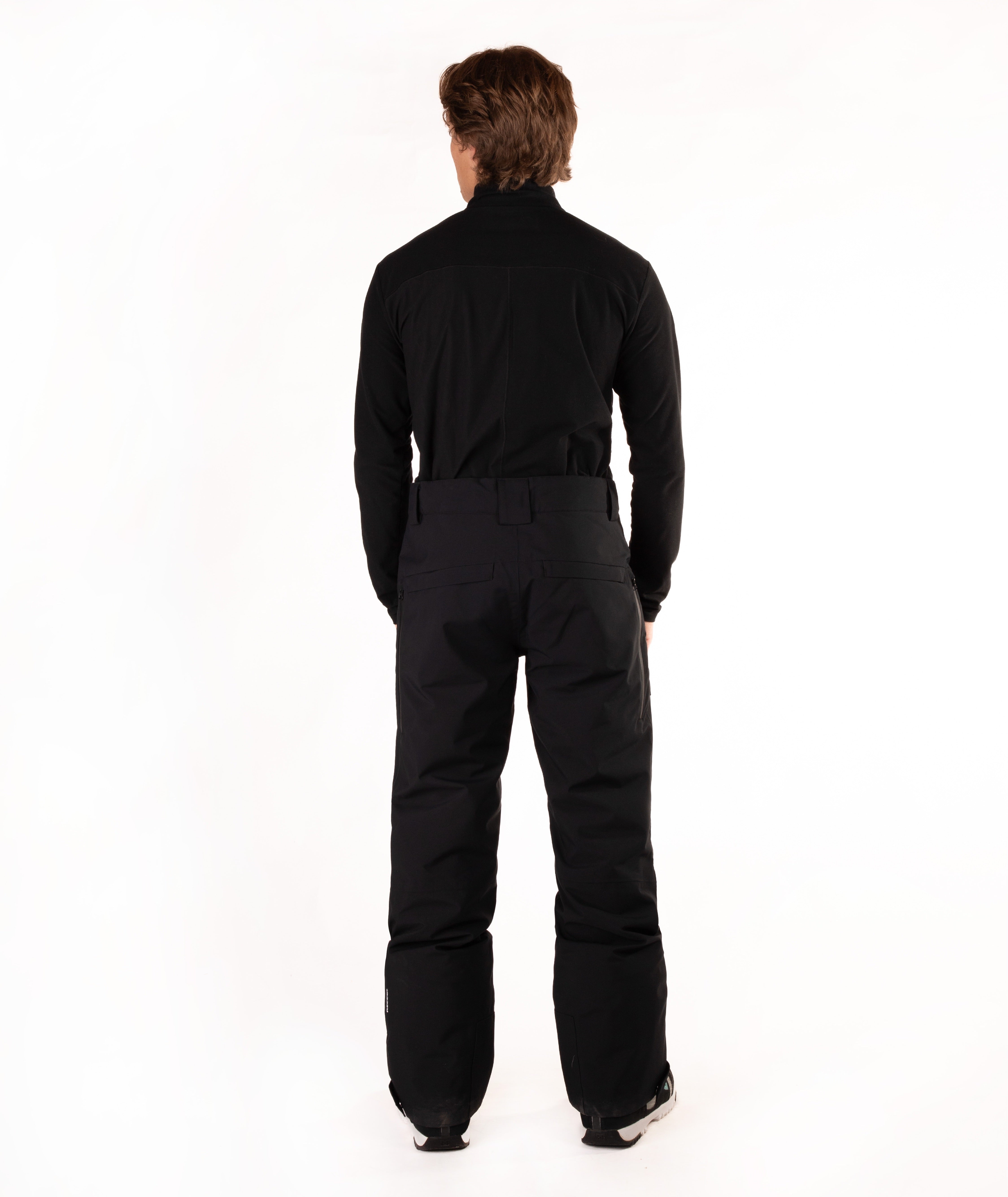 A man viewed from the back wearing a black long-sleeve top and black pants against a plain white studio background.