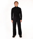 A man wearing a black long-sleeve half-zip athletic top and black ski pants, standing against a solid white studio background.