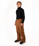 A man modeling a black long-sleeve quarter-zip fleece and brown ski pants against a solid white studio background.