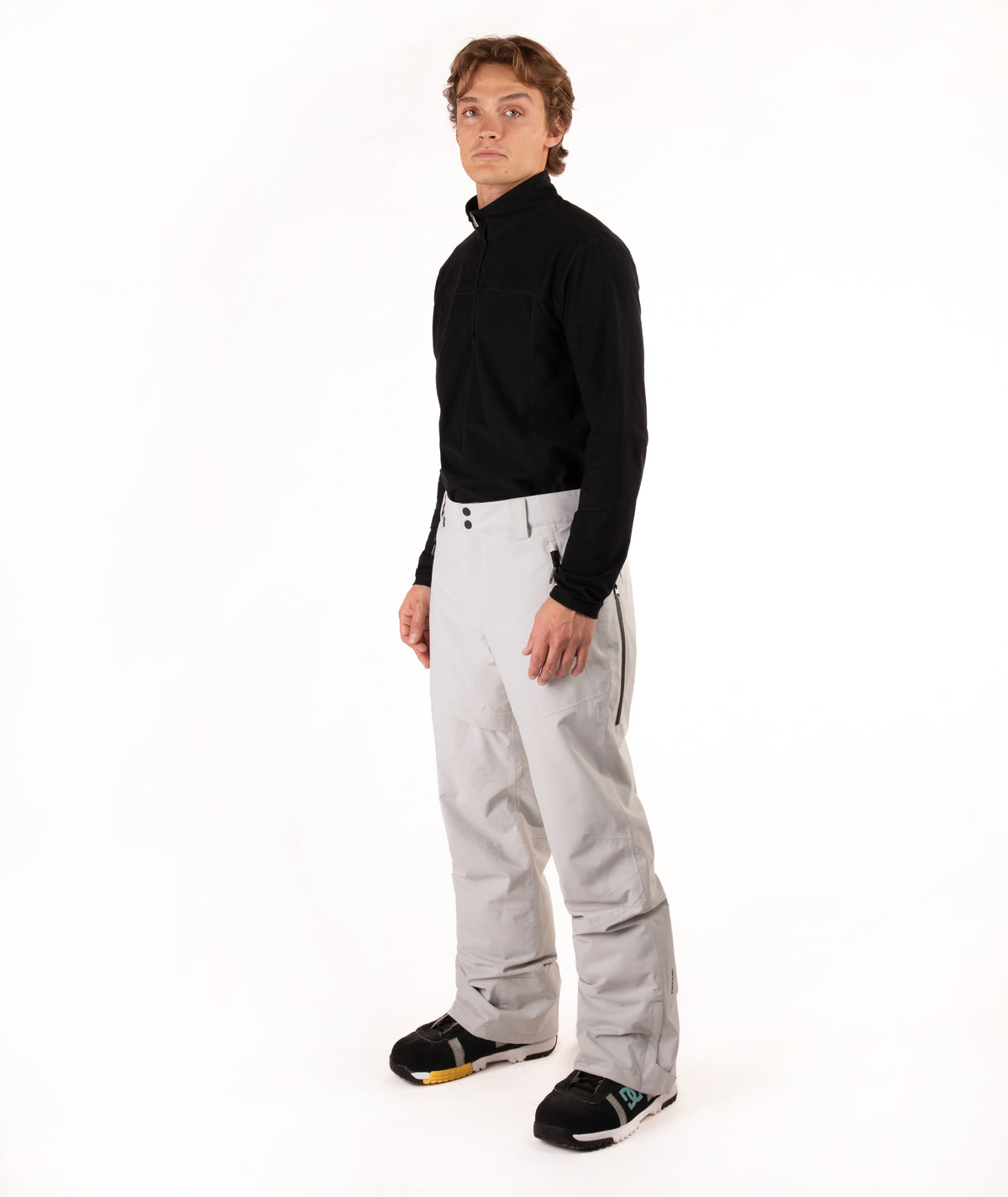A man modeling a black long-sleeve quarter-zip pullover and light gray snow pants against a plain white studio background.
