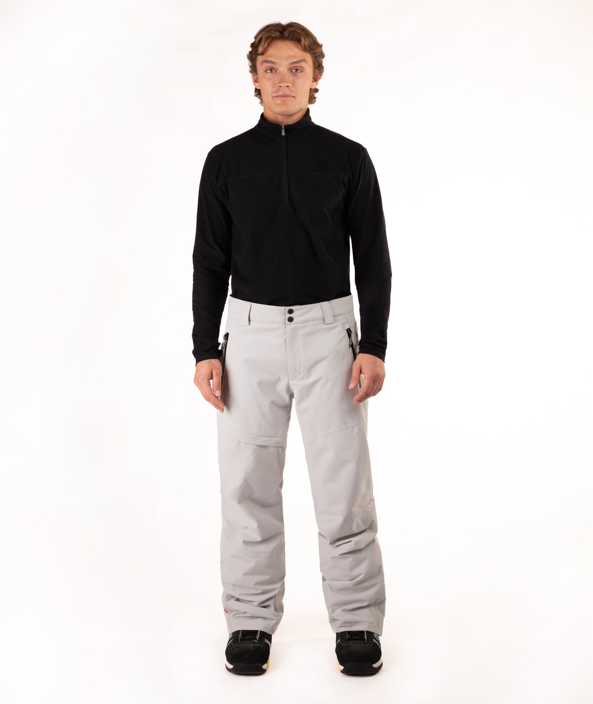 A man modeling a black long-sleeve quarter-zip pullover and light gray snow pants against a plain white studio background.