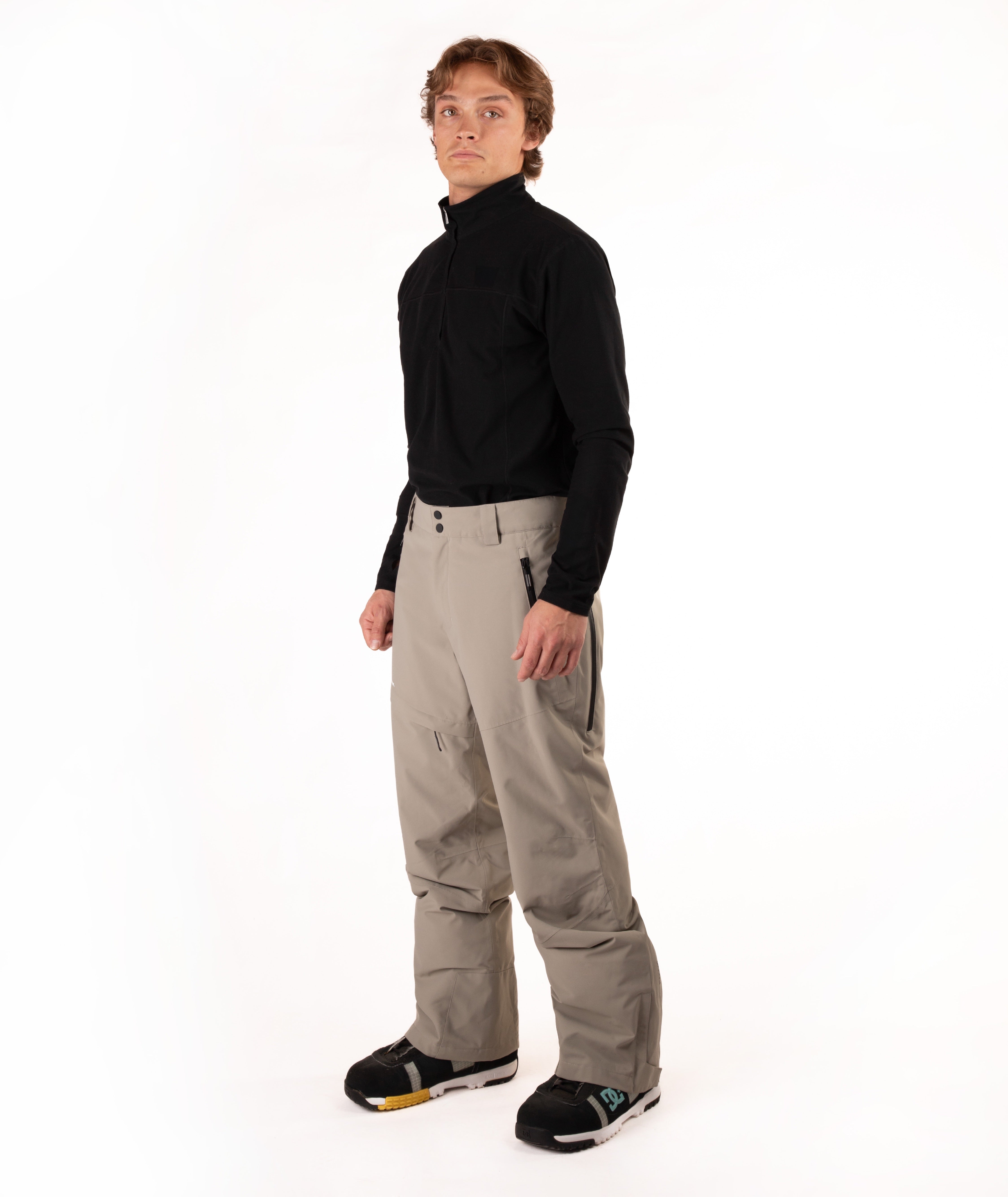 A man modeling a black long-sleeve quarter-zip fleece and beige ski pants against a white studio background.