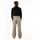 A man viewed from behind wearing a black long-sleeve shirt and beige snowboard pants against a white studio background.