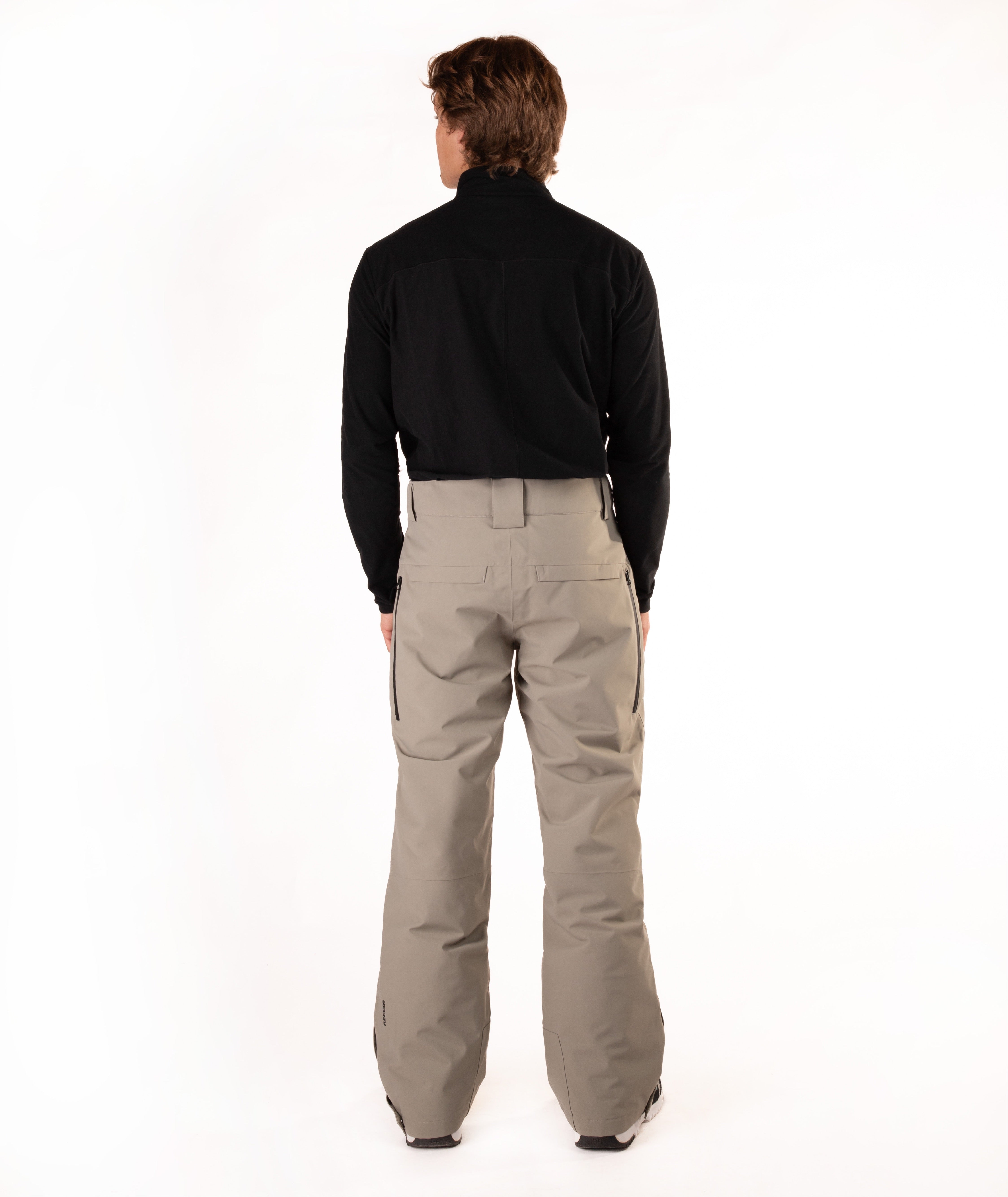 A man viewed from behind wearing a black long-sleeve shirt and beige snowboard pants against a white studio background.