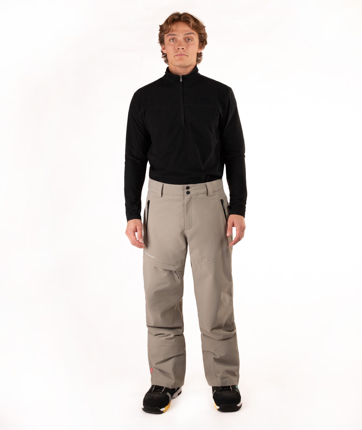 A man modeling a black long-sleeve quarter-zip fleece and beige ski pants against a white studio background.