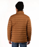 A man viewed from the back wearing a brown horizontal-quilted puffer jacket, a black knit beanie, and blue jeans against a plain white studio background.
