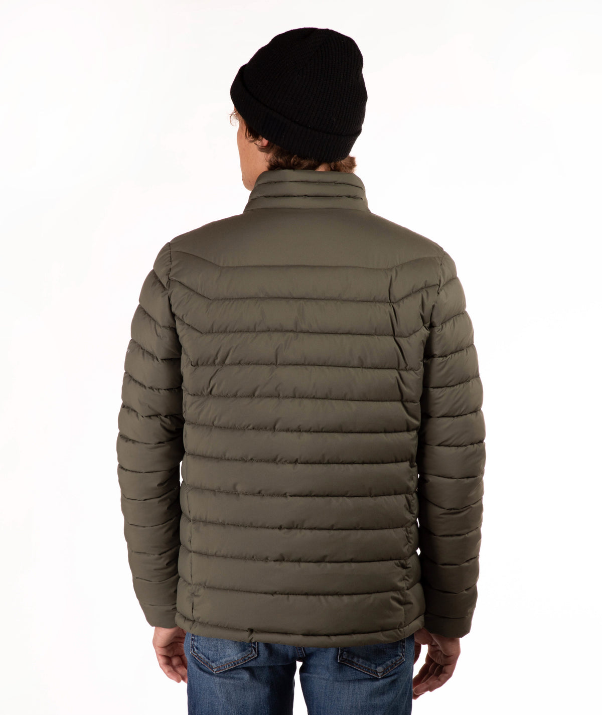A man viewed from the back wearing an olive green puffer jacket, a black knit beanie, and blue jeans against a plain white background.