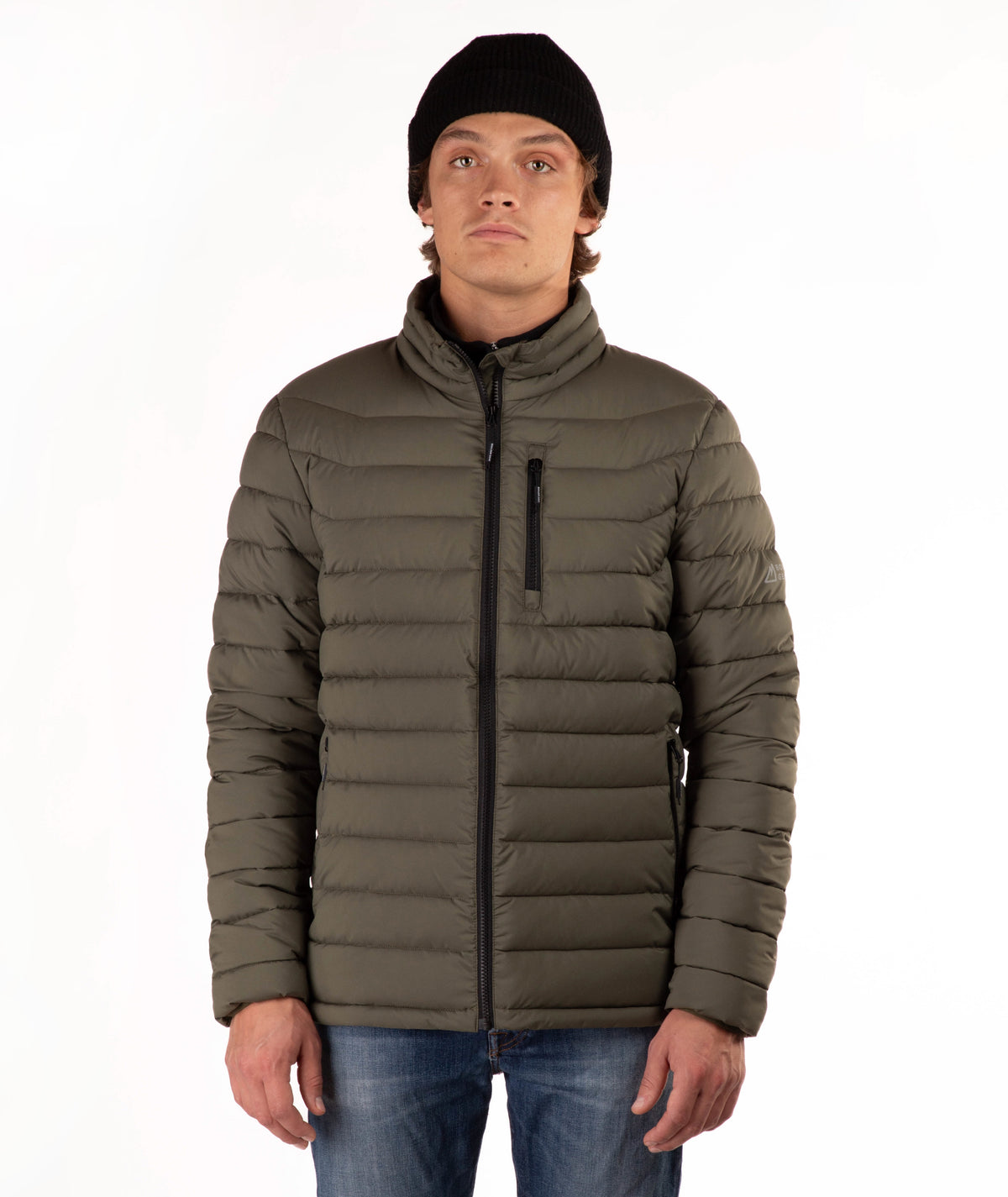 A man wearing a dark olive green puffer jacket with a black zipper, a black beanie, and blue jeans, standing against a plain white background.