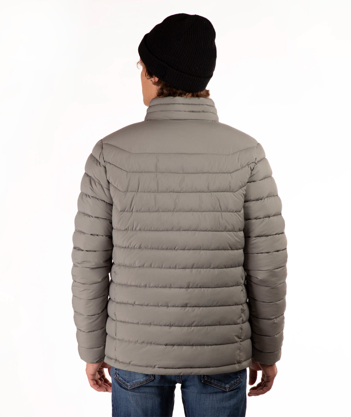 A person shown from the back wearing a taupe quilted puffer jacket, a black knit beanie, and blue jeans against a plain white studio background.