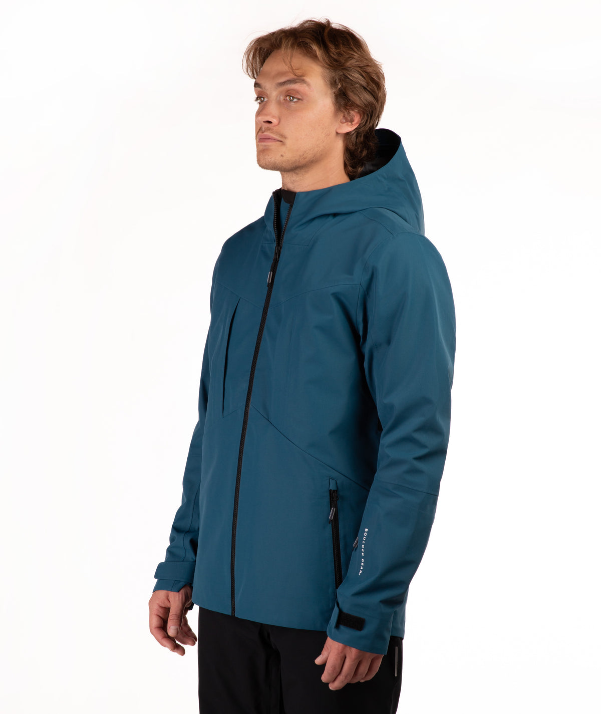 A man wearing a teal blue hooded jacket with black zippers, shown in profile against a plain white studio background.