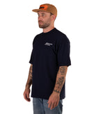 Man wearing a navy t-shirt with a logo and a brown cap on a white background