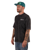 Man wearing a faded black t-shirt with a logo and a green cap on a white background