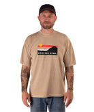 Man wearing a beige t-shirt with a logo and text, standing against a white background