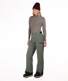 Person wearing a gray long-sleeve top and green snow pants on a white background