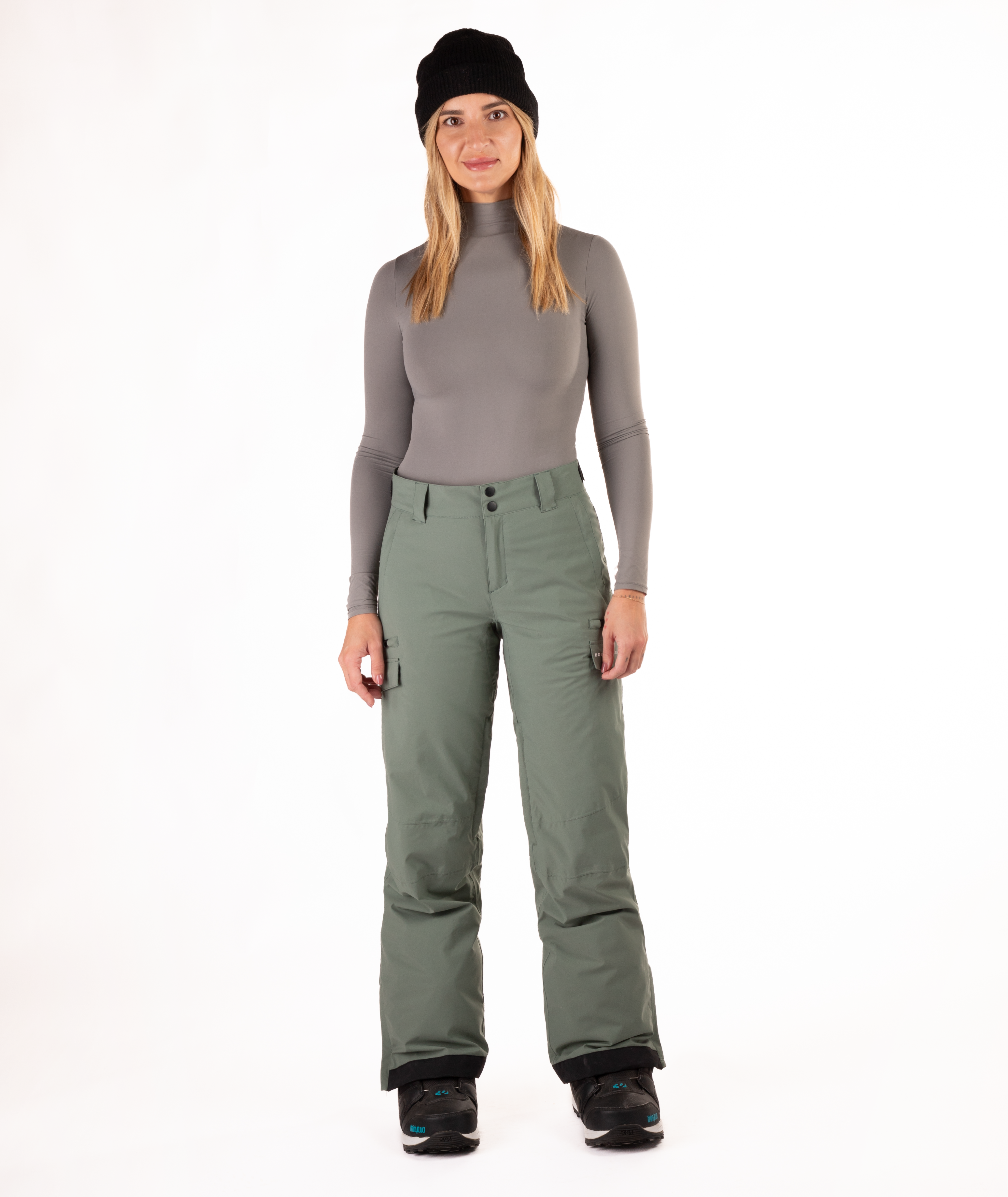 Person wearing a gray long-sleeve top and green snow pants on a white background