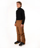 A man modeling a black long-sleeve quarter-zip top and brown snow pants with black snow shoes, standing against a solid white studio background.