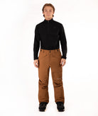 A man modeling a black long-sleeve quarter-zip top and brown snow pants with black snow shoes, standing against a solid white studio background.