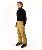 A man modeling a black long-sleeve quarter-zip fleece and mustard yellow snow pants with black snow boots, standing against a solid white studio background.