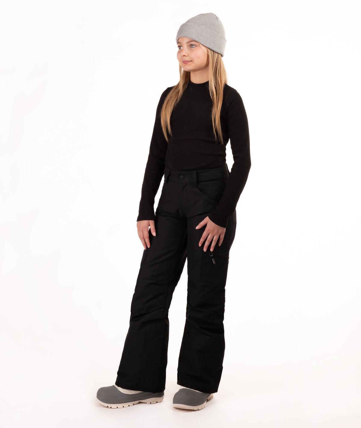 A young girl modeling a black long-sleeve top, black snow pants, a light gray beanie, and gray boots against a plain white studio background.