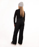 A girl shown from the back wearing a light gray beanie, a black long-sleeve top, black pants, and gray sneakers, standing against a plain white studio background.