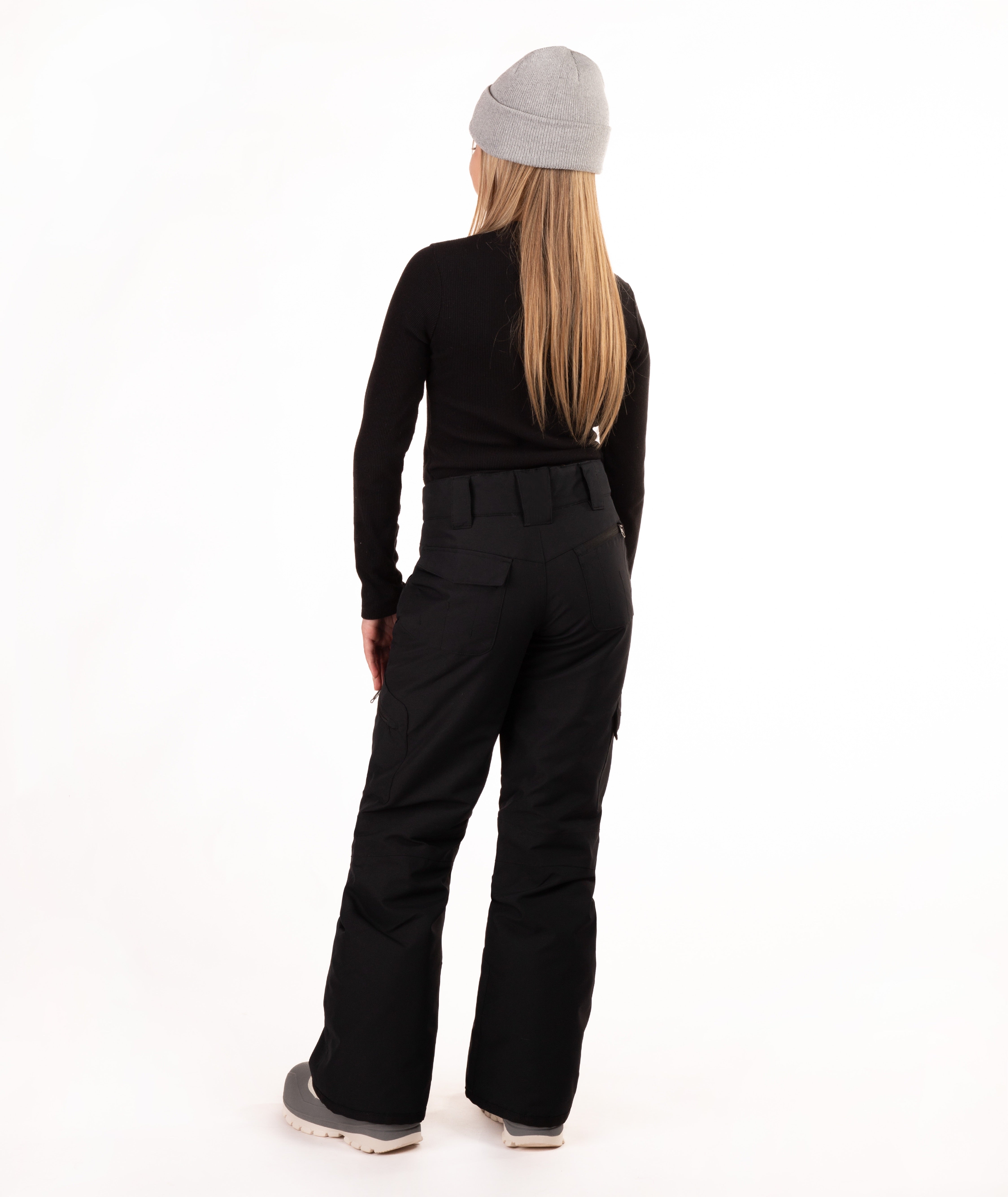 A girl shown from the back wearing a light gray beanie, a black long-sleeve top, black pants, and gray sneakers, standing against a plain white studio background.
