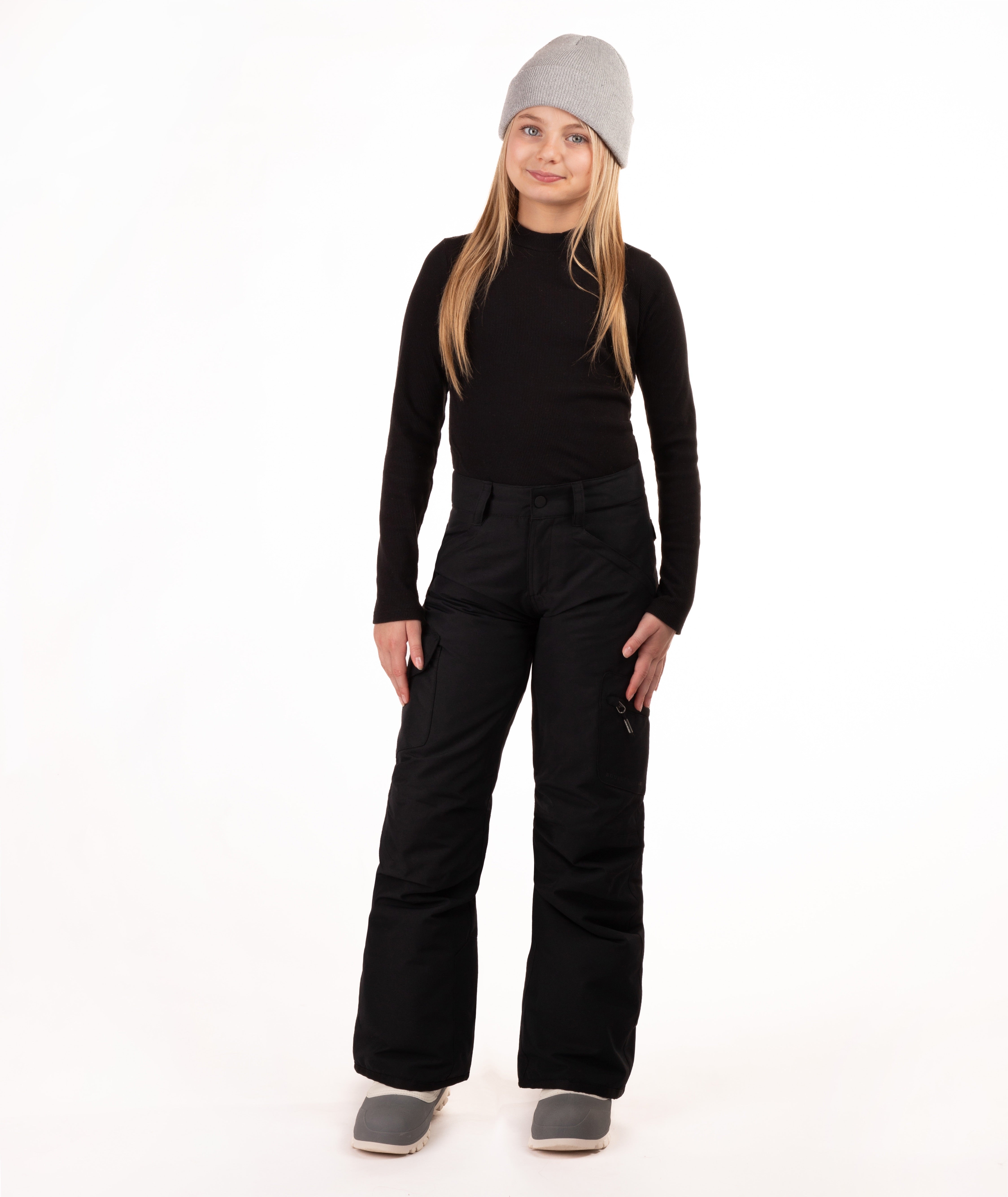 A young girl modeling a black long-sleeve top, black snow pants, a light gray beanie, and gray boots against a plain white studio background.
