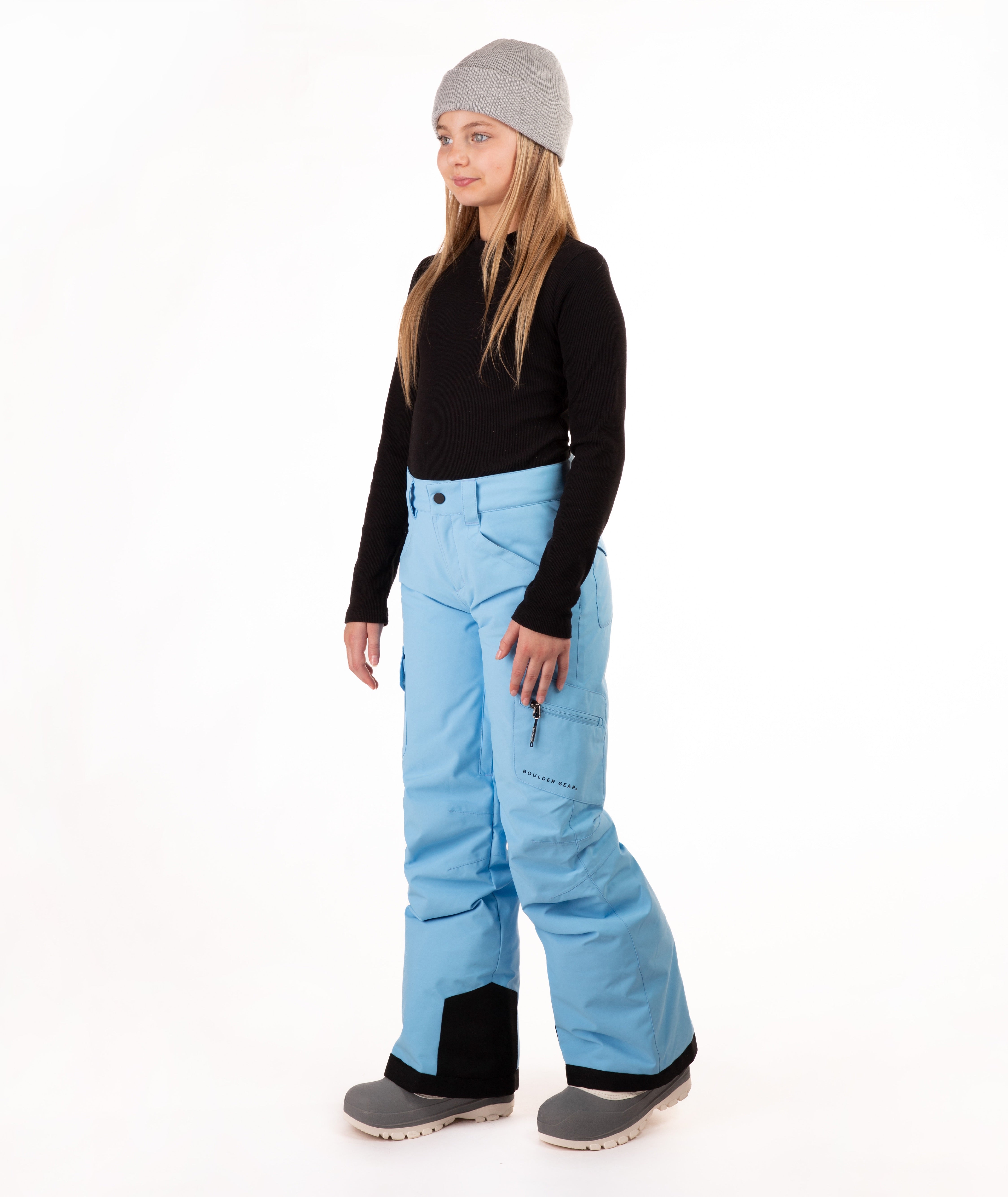 A young girl modeling a pair of light blue ski pants, a black long-sleeve top, and a gray beanie against a white studio background.