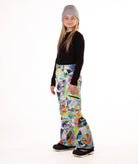 Girl wearing multi colored geometric patterned snow pants and a black top on a white background