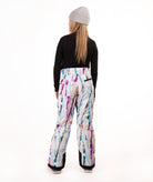 A model shown from the back wearing  snow pants with a colorful paint-splatter pattern, a black long-sleeve top, and a gray beanie against a white studio background.