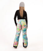 A person shown from the back wearing colorful snow pants with a pastel tie-dye pattern, a black long-sleeve top, and a gray beanie against a plain white studio background.