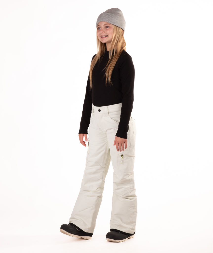 girl wearing cream colored snow pants and a black long-sleeve top on a white background