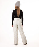 back of a girl wearing cream colored snow pants and a black long-sleeve top on a white background