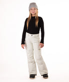 girl wearing cream colored snow pants and a black long-sleeve top on a white background