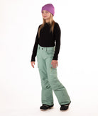 girl wearing green snow pants and a black long-sleeve top on a white background