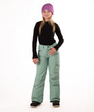 girl wearing green snow pants and a black long-sleeve top on a white background