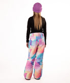 back of girl wearing multi color pastel abstract print snow pants and a black long-sleeve top on a white background