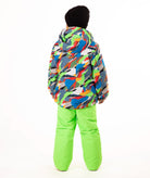 A child wearing a colorful camouflage-patterned ski jacket and bright neon green snow pants, standing against a plain white studio background.