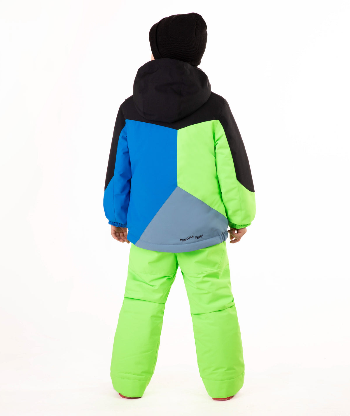 A child wearing a color-blocked ski jacket and matching snow pants, standing against a plain white studio background. The jacket has black, blue, and neon green panels, and the pants are bright neon green.