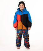 A young child wearing a color-blocked ski jacket in blue, red, black, and orange, paired with patterned snow pants and a black beanie, standing against a white studio background.