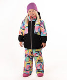 A young girl wearing a colorful abstract print ski jacket and matching pants, a purple beanie, and pink boots, standing against a white studio background.