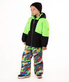 A child wearing a bright neon green and black ski jacket with colorful camouflage snow pants, a black beanie, and ski boots, standing against a plain white background.