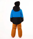 A child standing against a white studio background wearing a color-blocked ski jacket in blue and black, brown snow pants, and a black beanie