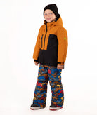 A child wearing a kids' ski jacket and snow pants set against a plain white background. The jacket is a colorblock design in brown and black, paired with blue snow pants featuring a multicolor mountain and ski pattern.