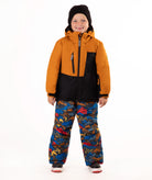 A child wearing a kids' ski jacket and snow pants set against a plain white background. The jacket is a colorblock design in brown and black, paired with blue snow pants featuring a multicolor mountain and ski pattern.
