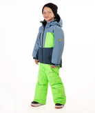 A child wearing a color-blocked ski jacket in slate blue, navy, and neon green, paired with neon green ski pants, a black beanie, standing against a white studio background.