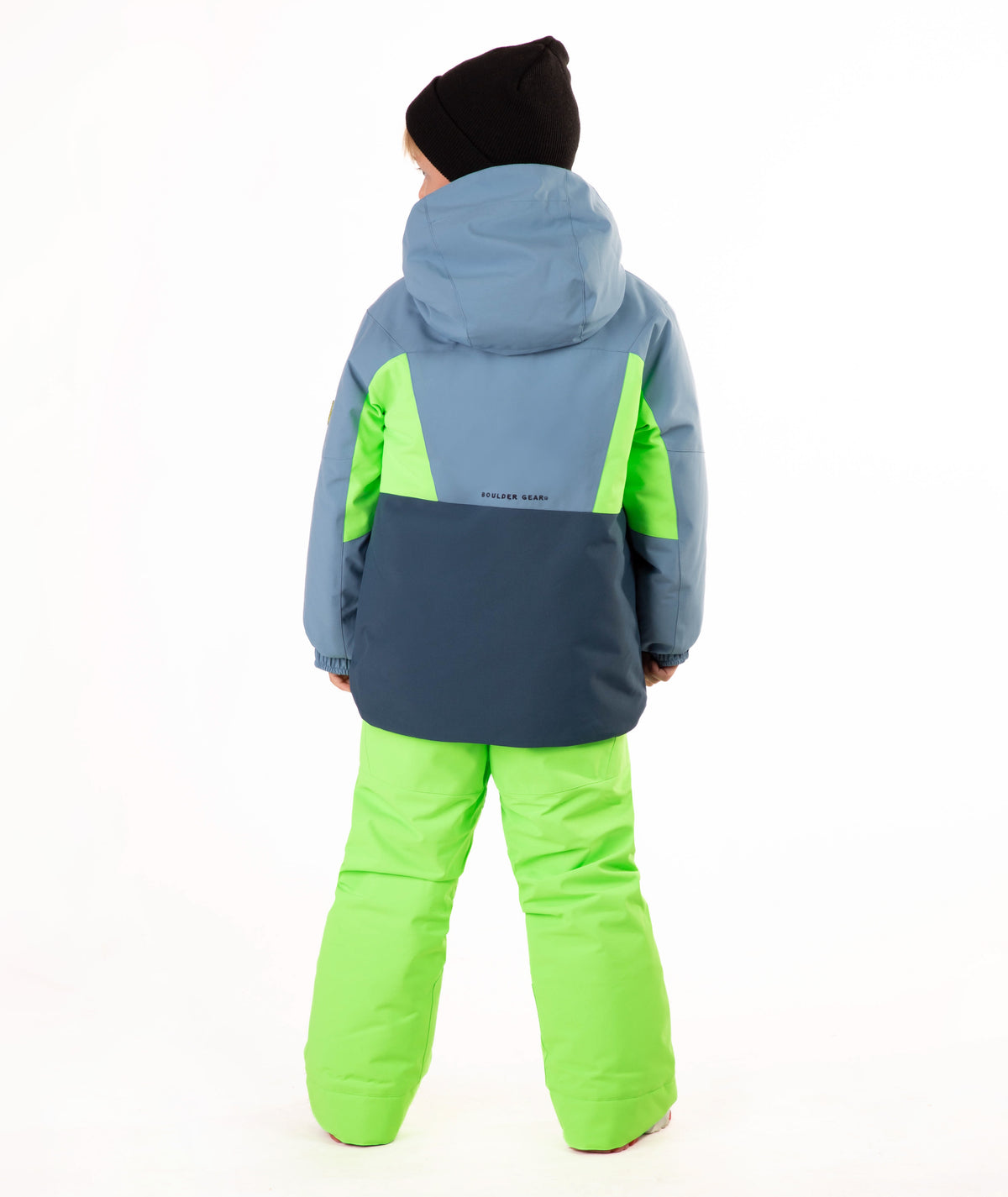 A child wearing a color-blocked ski jacket in slate blue, navy, and neon green, paired with neon green ski pants, a black beanie, standing against a white studio background.