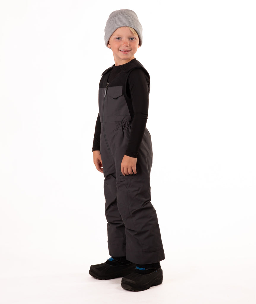Child wearing dark gray snow bibs on a white background