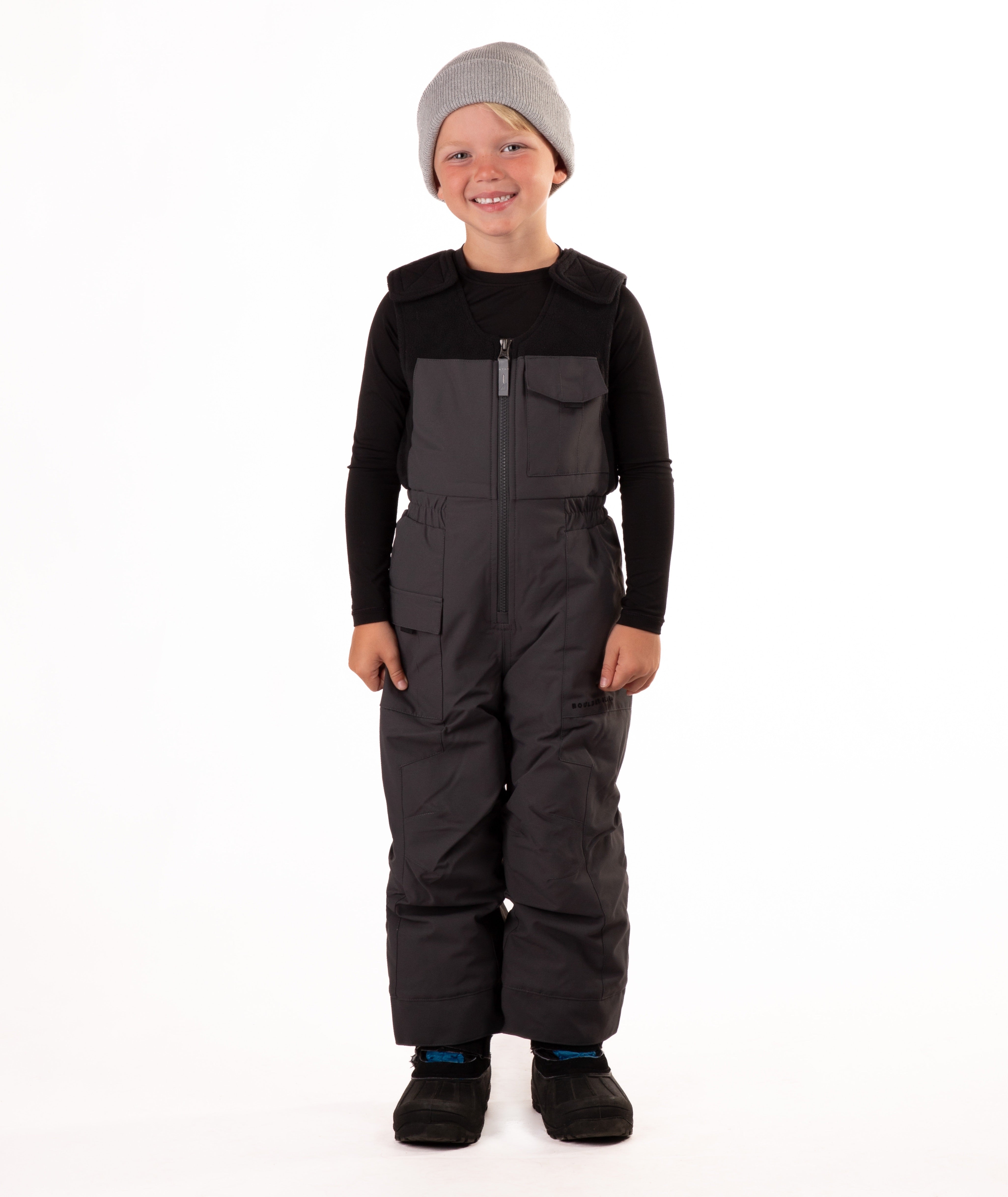 Child wearing dark gray snow bibs on a white background