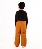 A child wearing a black knit beanie, a black long-sleeve top, and rust colored snow bib overalls, standing against a plain white background.