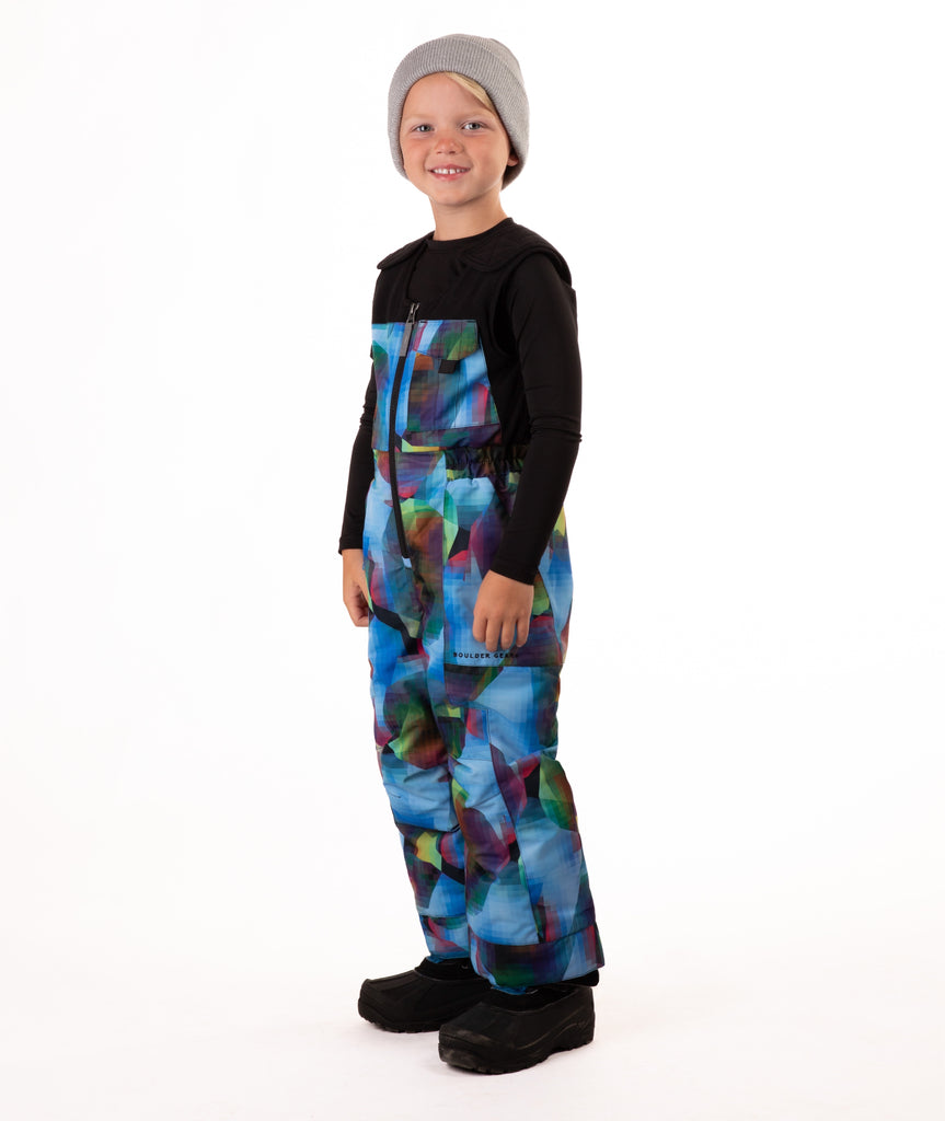 Child wearing colorful geometric print snow bibs on a white background